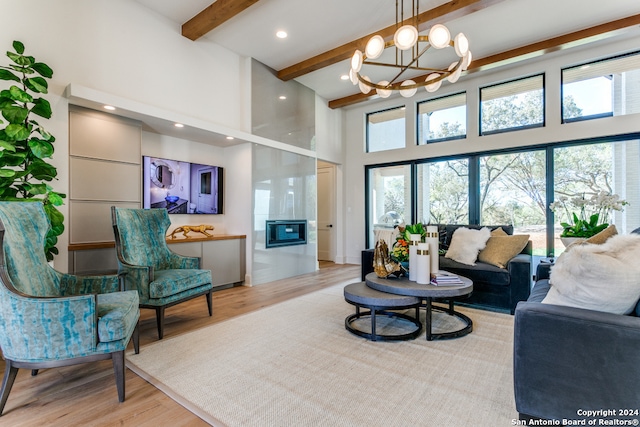 living room with a towering ceiling, light hardwood / wood-style flooring, a chandelier, and beamed ceiling