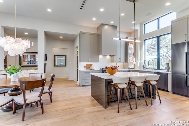 kitchen with gray cabinetry, appliances with stainless steel finishes, a kitchen island, light hardwood / wood-style floors, and decorative light fixtures