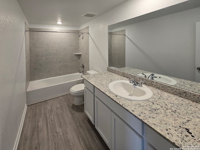 full bathroom with tiled shower / bath combo, vanity, hardwood / wood-style flooring, and toilet