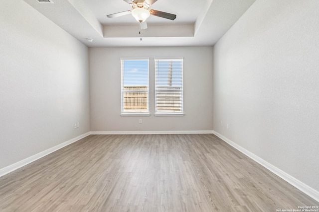 unfurnished room featuring light hardwood / wood-style flooring, ceiling fan, and a raised ceiling