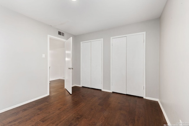 unfurnished bedroom with multiple closets and dark hardwood / wood-style flooring