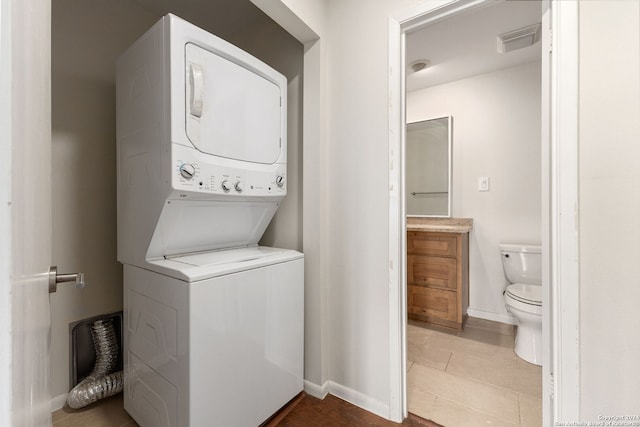 laundry area with stacked washer / drying machine and tile patterned floors