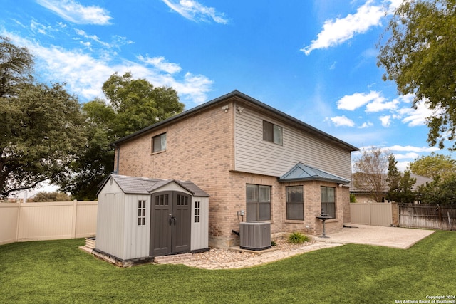 rear view of property with a yard, a patio area, a storage unit, and central air condition unit