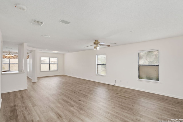 empty room featuring a textured ceiling, ceiling fan with notable chandelier, and light wood-type flooring