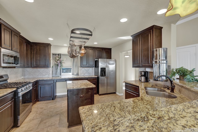 kitchen with dark brown cabinets, light stone counters, a kitchen island, sink, and stainless steel appliances