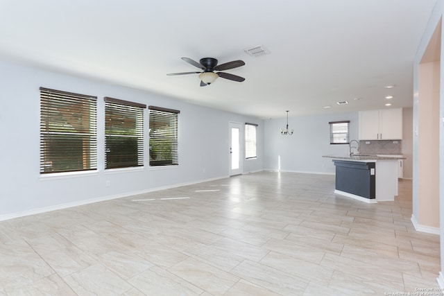 unfurnished living room featuring sink, plenty of natural light, and ceiling fan with notable chandelier