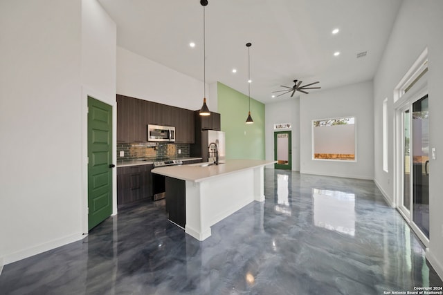 kitchen with decorative backsplash, appliances with stainless steel finishes, a kitchen island with sink, dark brown cabinetry, and decorative light fixtures