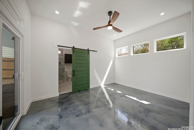 unfurnished bedroom featuring ensuite bathroom, a barn door, and ceiling fan