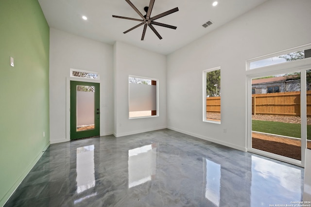 unfurnished room with ceiling fan, a towering ceiling, and concrete flooring