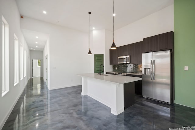 kitchen with decorative backsplash, an island with sink, hanging light fixtures, stainless steel appliances, and dark brown cabinetry