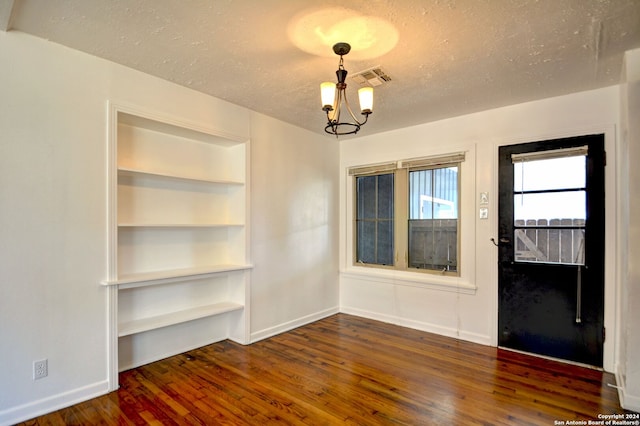 unfurnished dining area with a textured ceiling, built in shelves, an inviting chandelier, and dark hardwood / wood-style flooring