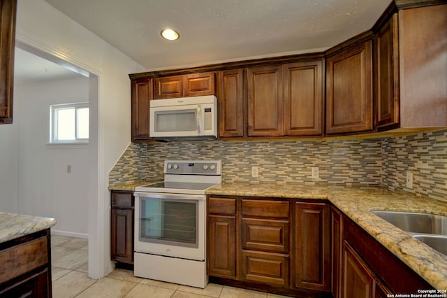 kitchen with backsplash, light tile patterned flooring, light stone countertops, and white appliances