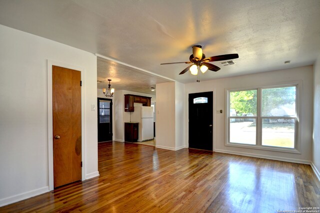 unfurnished living room featuring a textured ceiling, dark hardwood / wood-style floors, and ceiling fan with notable chandelier