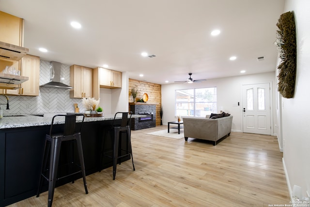 kitchen with a kitchen bar, light stone counters, wall chimney range hood, and light hardwood / wood-style floors