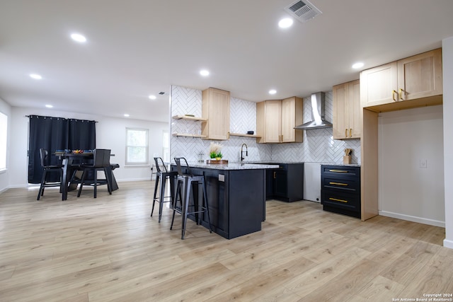 kitchen featuring a kitchen island, wall chimney exhaust hood, a kitchen breakfast bar, light wood-type flooring, and light brown cabinetry