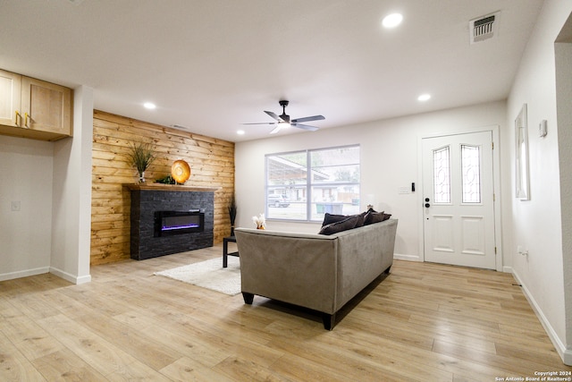 living room featuring ceiling fan, a fireplace, light wood-type flooring, and wood walls