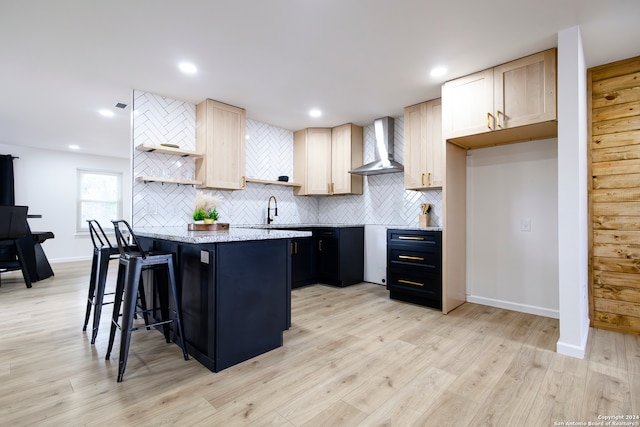 kitchen featuring decorative backsplash, a breakfast bar area, light brown cabinetry, light hardwood / wood-style floors, and wall chimney exhaust hood