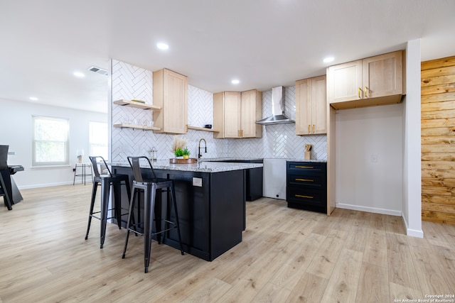 kitchen featuring a kitchen island, wall chimney exhaust hood, a kitchen breakfast bar, backsplash, and light hardwood / wood-style floors