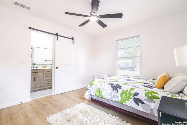 bedroom featuring light hardwood / wood-style flooring, ensuite bathroom, a barn door, and ceiling fan