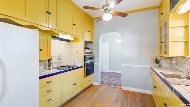 kitchen with backsplash, light hardwood / wood-style flooring, black appliances, tile counters, and sink