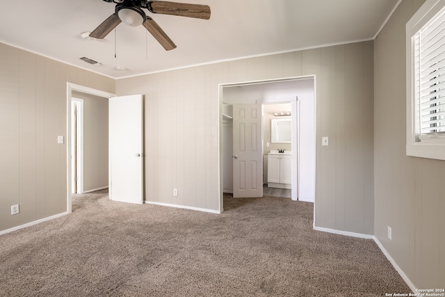 unfurnished bedroom with a closet, carpet, crown molding, ceiling fan, and wood walls