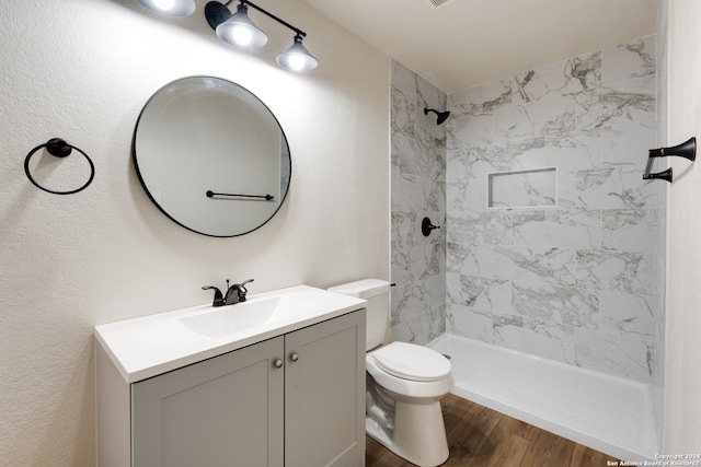 bathroom with toilet, hardwood / wood-style flooring, vanity, and tiled shower