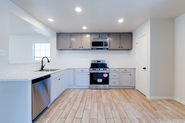 kitchen with sink, kitchen peninsula, stainless steel appliances, gray cabinets, and light hardwood / wood-style flooring