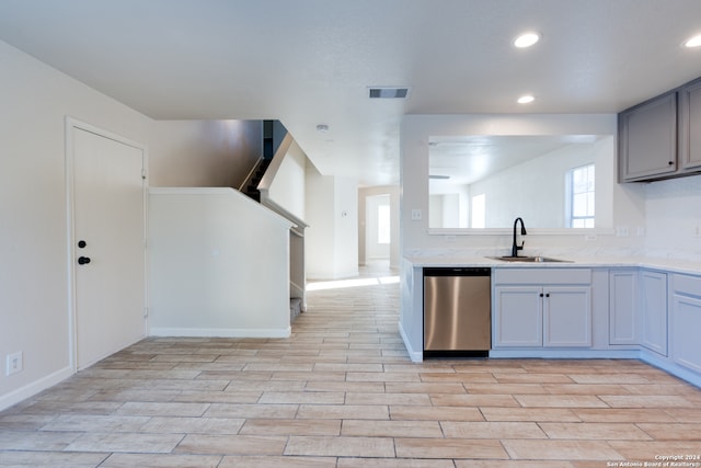 kitchen featuring sink, light wood-type flooring, stainless steel dishwasher, gray cabinets, and light stone counters