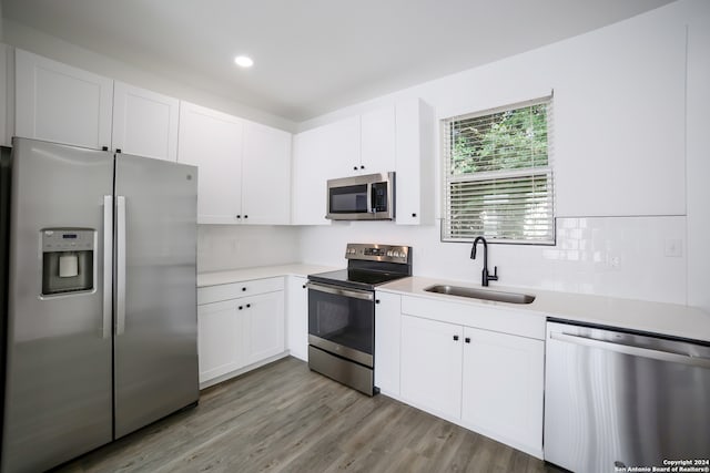 kitchen with stainless steel appliances, sink, white cabinets, light hardwood / wood-style floors, and tasteful backsplash