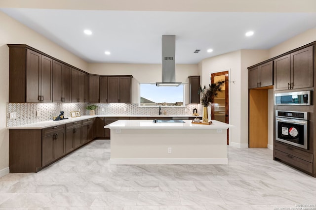 kitchen featuring appliances with stainless steel finishes, island exhaust hood, dark brown cabinets, a center island, and decorative backsplash