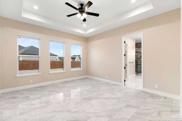 unfurnished room with ceiling fan and a tray ceiling