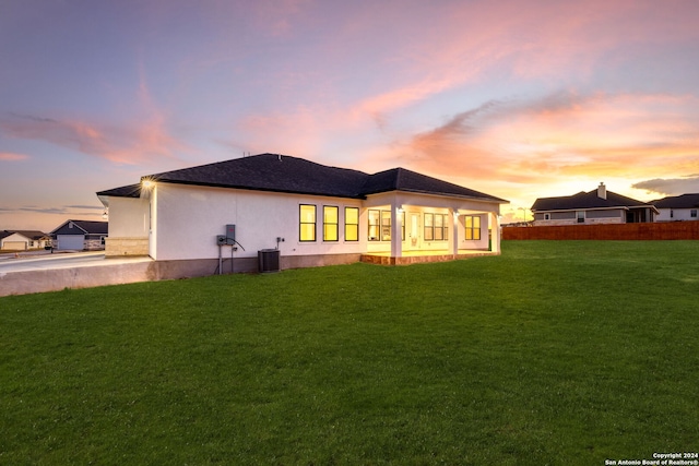 back house at dusk with central air condition unit and a lawn