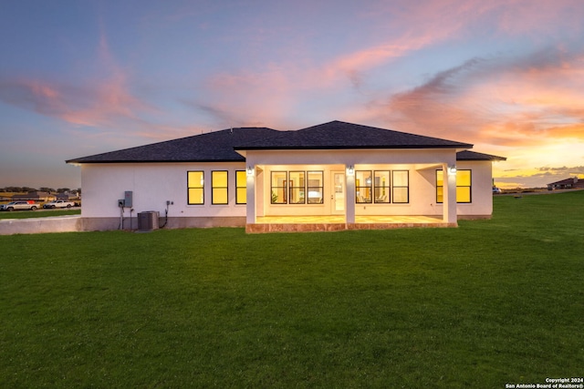 back house at dusk featuring a yard and central AC