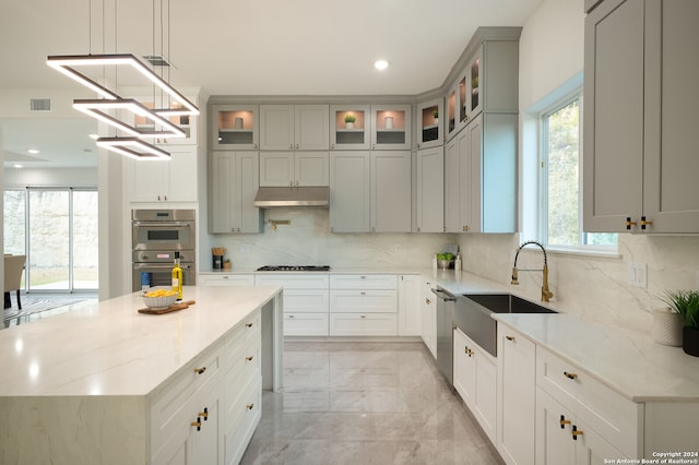 kitchen featuring light stone countertops, sink, a center island, backsplash, and appliances with stainless steel finishes