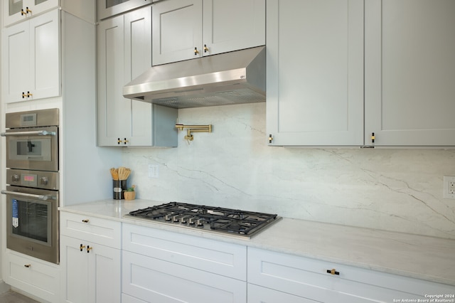 kitchen featuring tasteful backsplash, white cabinetry, light stone counters, and appliances with stainless steel finishes