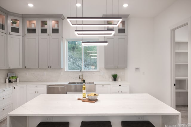 kitchen with a center island, hanging light fixtures, tasteful backsplash, light stone counters, and stainless steel dishwasher