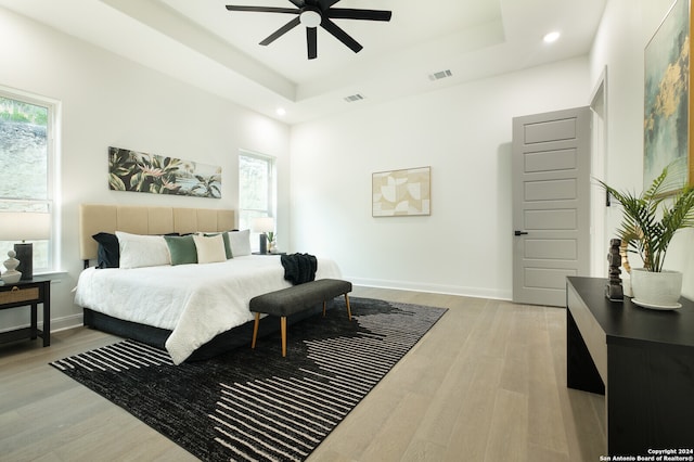 bedroom with light wood-type flooring, a raised ceiling, and ceiling fan