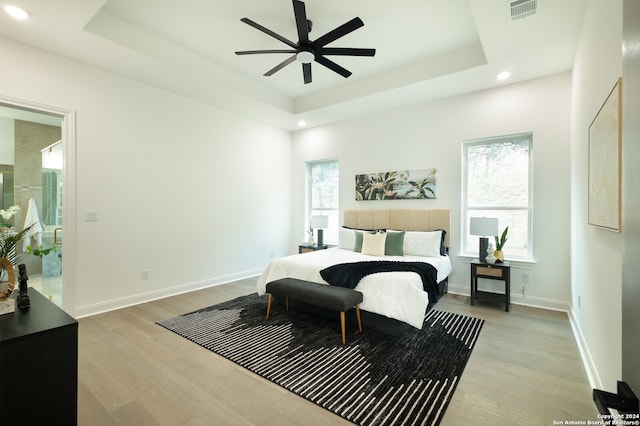 bedroom featuring connected bathroom, light hardwood / wood-style flooring, a raised ceiling, and ceiling fan