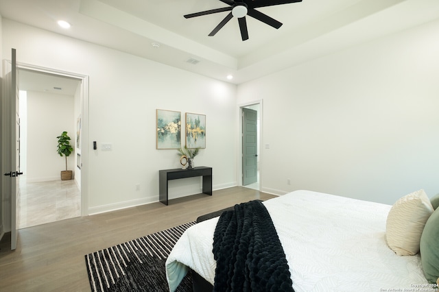 bedroom featuring a raised ceiling, ceiling fan, and light wood-type flooring