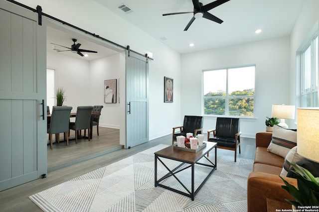 living room with a barn door, ceiling fan, and light hardwood / wood-style flooring