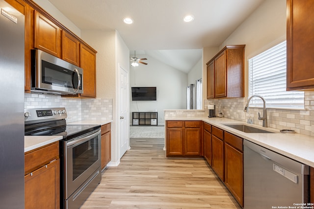 kitchen featuring tasteful backsplash, appliances with stainless steel finishes, sink, light hardwood / wood-style floors, and vaulted ceiling