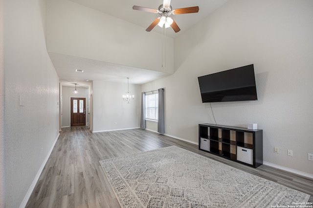 unfurnished living room with a towering ceiling, ceiling fan with notable chandelier, and hardwood / wood-style floors