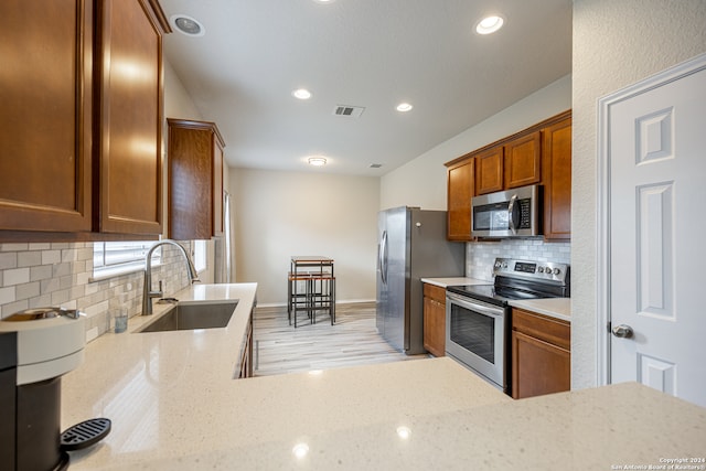 kitchen with sink, stainless steel appliances, light stone counters, decorative backsplash, and light hardwood / wood-style flooring