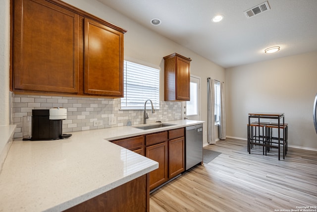 kitchen featuring sink, light hardwood / wood-style floors, stainless steel dishwasher, light stone counters, and decorative backsplash