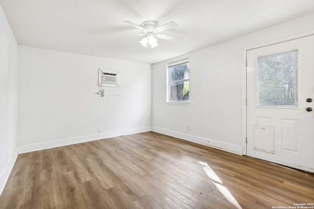 empty room featuring a wall mounted AC, hardwood / wood-style flooring, and ceiling fan