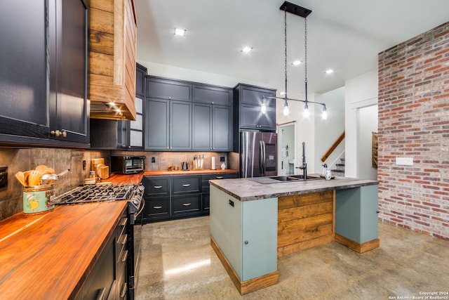 kitchen featuring tasteful backsplash, a kitchen island with sink, stainless steel appliances, decorative light fixtures, and butcher block countertops