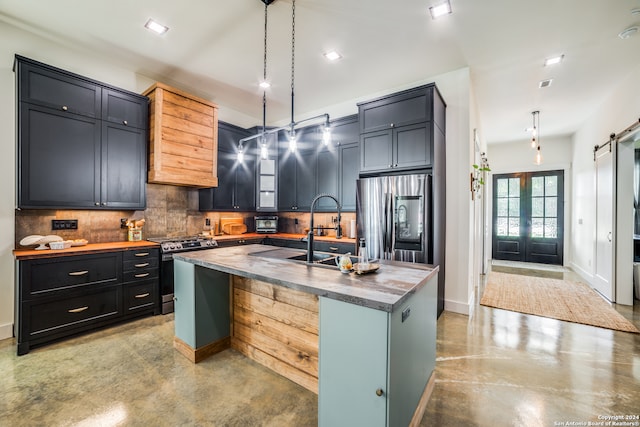 kitchen featuring decorative backsplash, a center island with sink, a barn door, pendant lighting, and stainless steel appliances