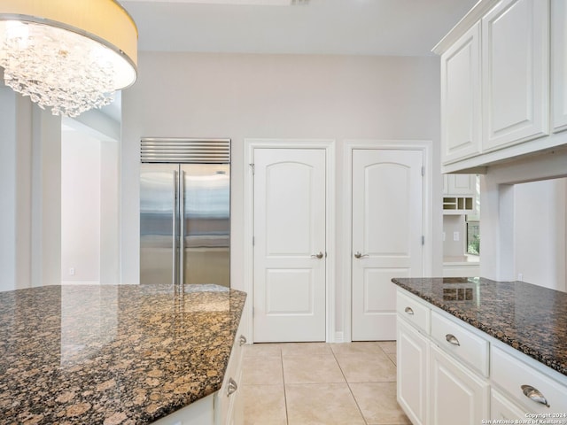 kitchen featuring stainless steel built in fridge, light tile patterned floors, white cabinetry, and dark stone counters