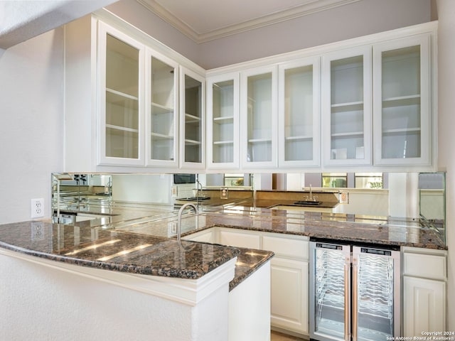 kitchen with kitchen peninsula, white cabinetry, dark stone counters, wine cooler, and ornamental molding