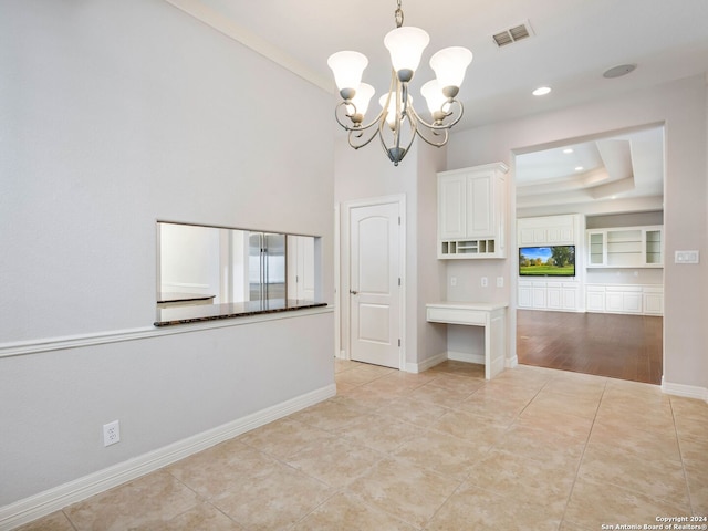 tiled spare room with a chandelier, built in shelves, and a raised ceiling